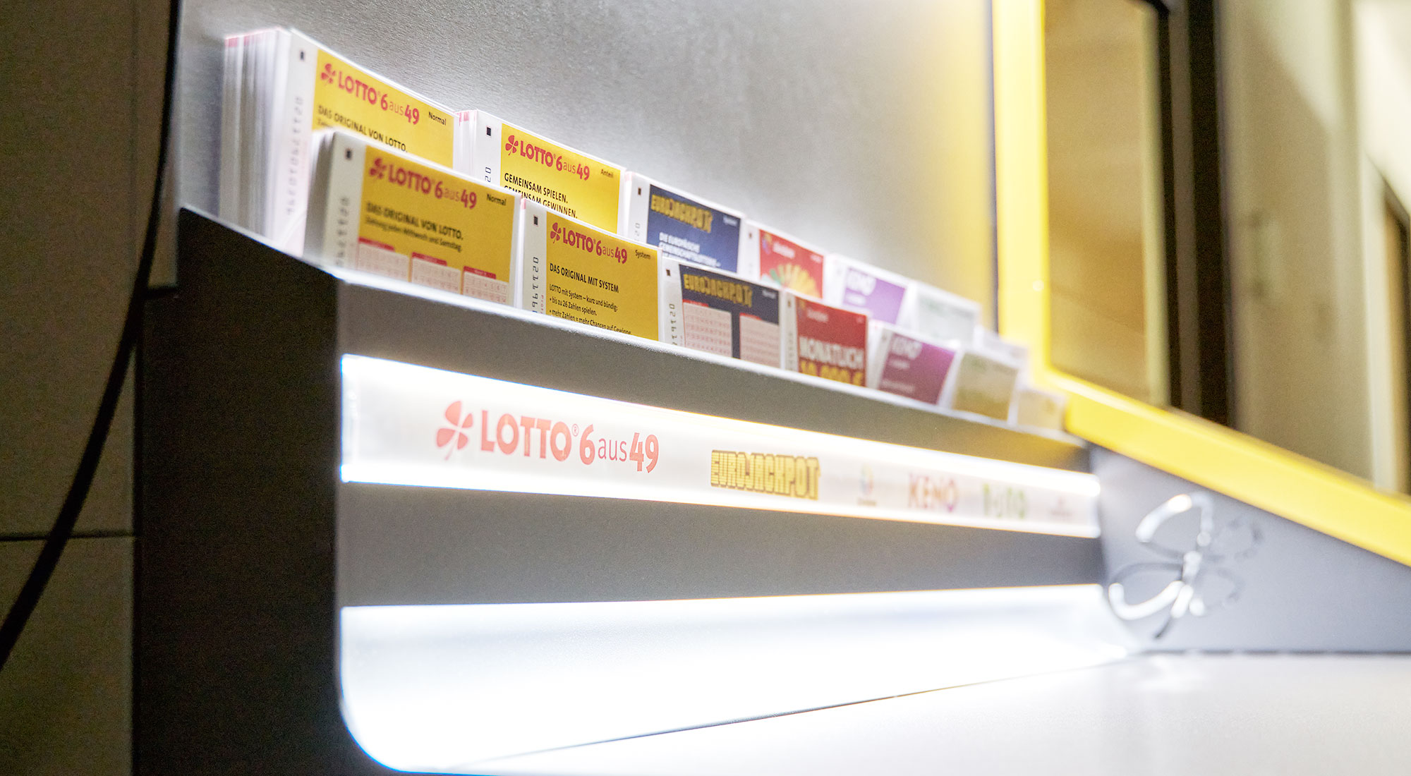 Spielscheine verschiedener Lotterieprodukte aus dem Sortiment der Staatlichen Lotterie- und Spielbankverwaltung einsortiert in eine sogenannte Lottowand als typische Präsentationsform in Annahmestellen.